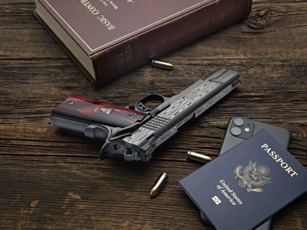 CABOT GUN OF THE MONTH 2023 JUNE 1911 BEDSIDE DEMON 9MM LEFT SIDE VIEW LAYING FLAT WITH BOOK AND ITEMS
